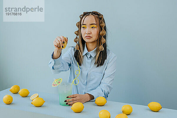 Nachdenkliche Frau drückt Zitrone in Cocktail vor blauem Hintergrund