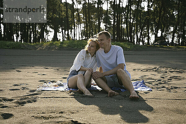 Happy couple sitting at beach on sunny day