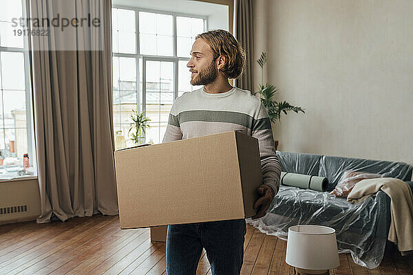Junger Mann mit Karton steht im Wohnzimmer