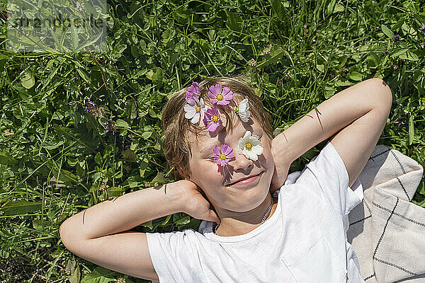 Fröhlicher Junge mit Blumen auf Stirn und Augen an einem sonnigen Tag