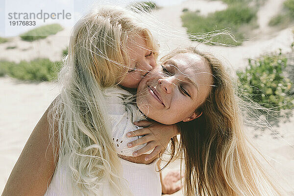 Liebevolle Tochter umarmt und küsst Mutter am Strand auf die Wange
