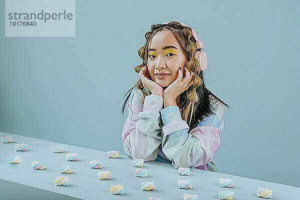 Young woman wearing headphones sitting at table with marshmallows in studio