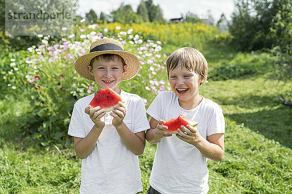 Fröhliche Jungs mit Wassermelonenscheiben stehen im Garten