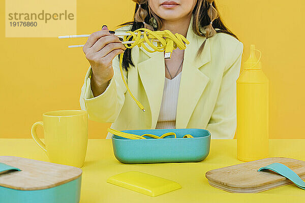 Junge Frau hält verdrahtete Nudeln in Essstäbchen vor gelbem Hintergrund