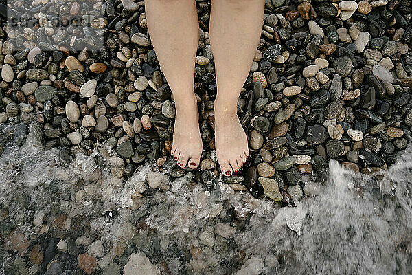 Beine einer Frau am Kiesstrand am Meer