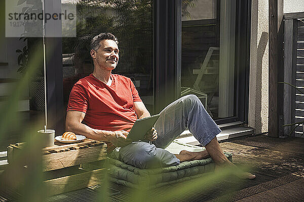 Mann entspannt sich auf Balkon mit digitalem Tablet in der Hand