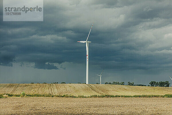 Wind turbines on field under cloudy sky