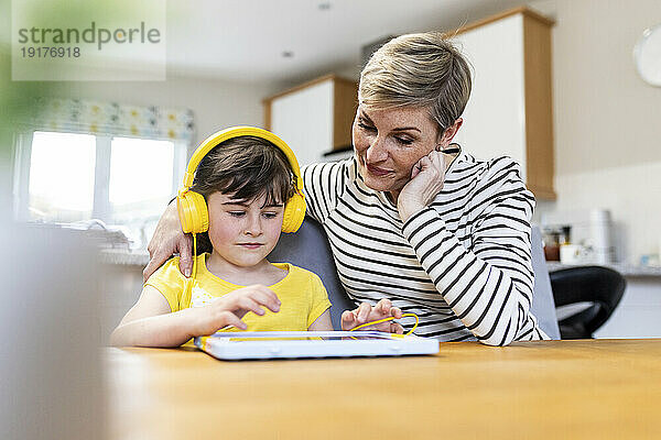 Mädchen beim E-Learning auf einem Tablet-PC  während ihre Mutter zu Hause sitzt