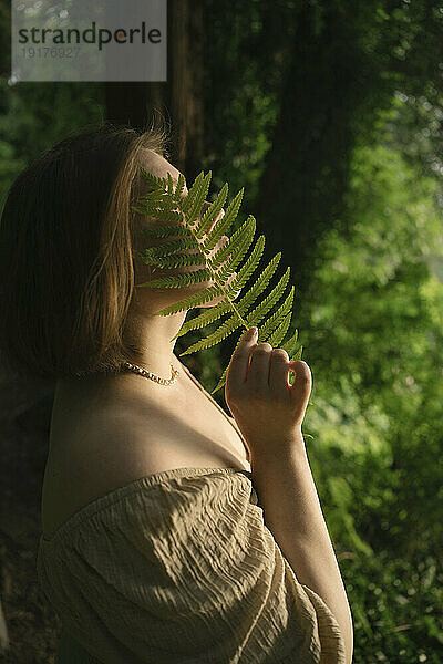 Young woman covering face with fern leaf in garden