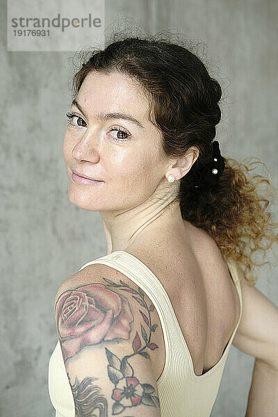 Lächelnde Frau mit Tattoo vor Betonwand