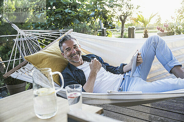 Smiling mature man with tablet PC lying in hammock