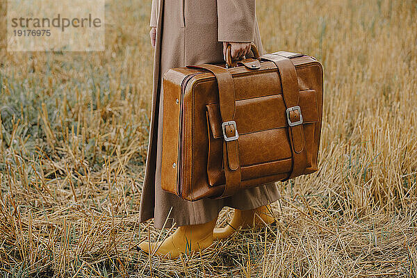 Frau mit braunem Koffer im Retro-Stil im Feld