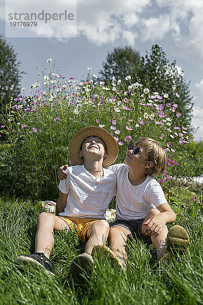Fröhliche Jungs sitzen an sonnigen Tagen auf Gras im Garten