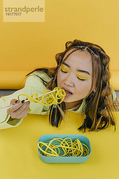 Young woman eating wired noodles at table in studio
