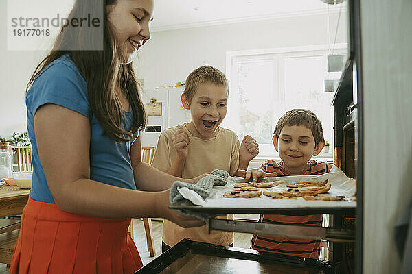 Happy brothers with sister preparing pizzas in oven at home