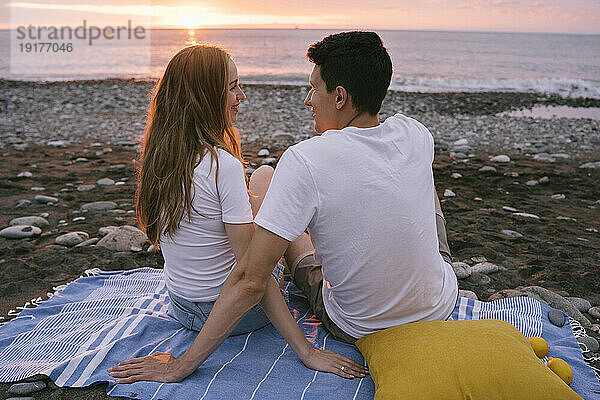 Lächelndes junges romantisches Paar  das sich im Urlaub am Strand unterhält