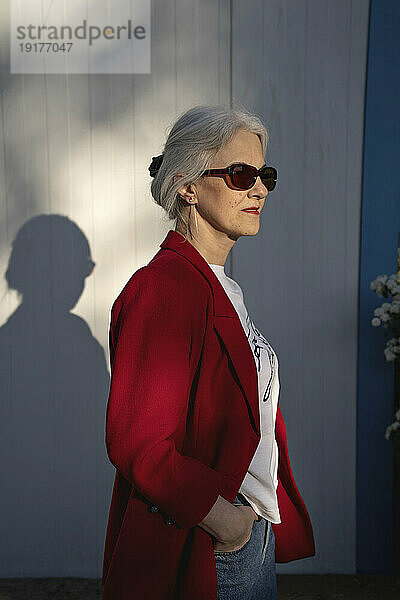 Selbstbewusste Frau mit Hand in der Tasche und Sonnenbrille in der Nähe der Wand