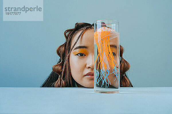 Junge Frau bedeckt ihr halbes Gesicht mit einer Qualle im Glas