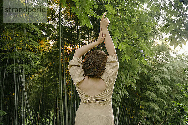 Junge Frau mit erhobenen Armen steht neben Bambuspflanzen
