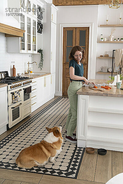 Frau schneidet Gemüse und schaut Hund in der Küche an