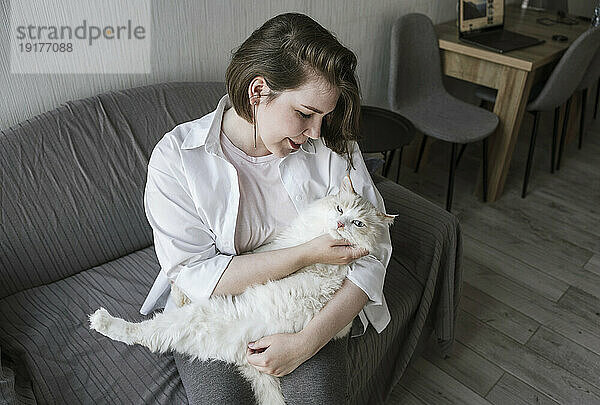 Junge Frau streichelt Katze auf Sofa