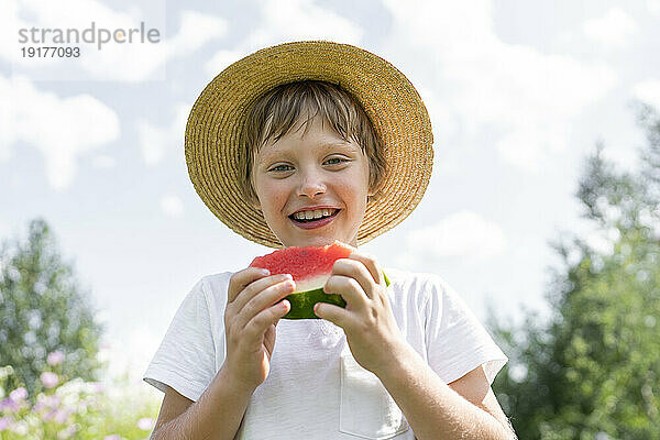 Glücklicher Junge  der mit einer Scheibe Wassermelone steht
