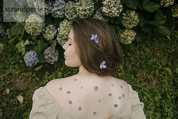 Young woman with flower petals on back in garden