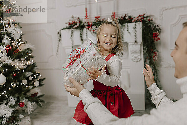 Glückliche Tochter hält Geschenk in der Nähe des Weihnachtsbaums