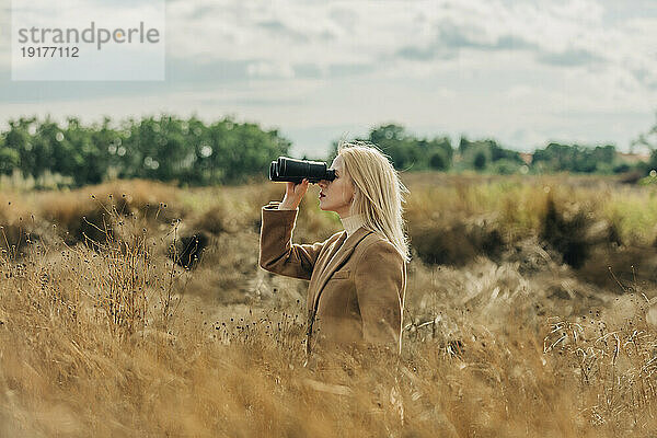 Blonde Frau schaut durch ein Fernglas im Weizenfeld