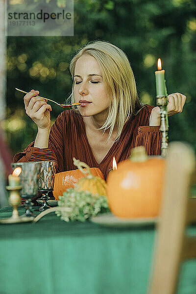 Blonde Frau mit geschlossenen Augen riecht Kürbissuppe am Esstisch