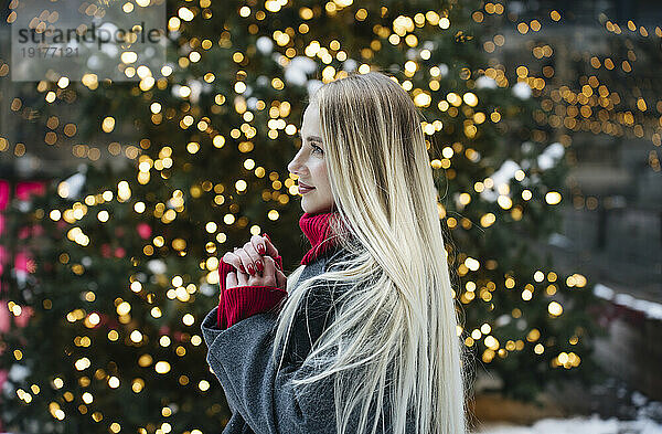 Glückliche blonde Frau  die vor dem Weihnachtsbaum steht