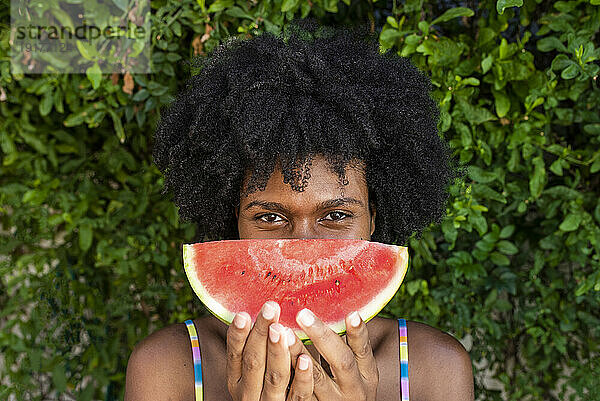 Junge Frau mit einer Scheibe Wassermelone vor Pflanzen