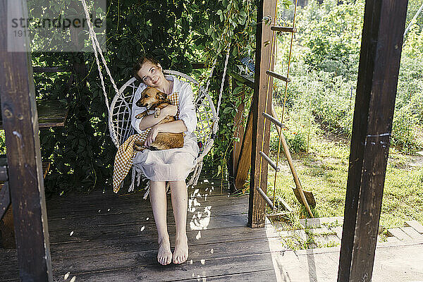 Relaxed woman with dog swinging on swing in garden