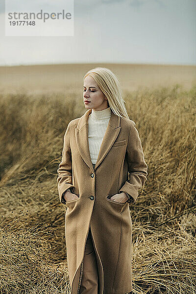 Blonde Frau mit geschlossenen Augen steht auf dem Feld