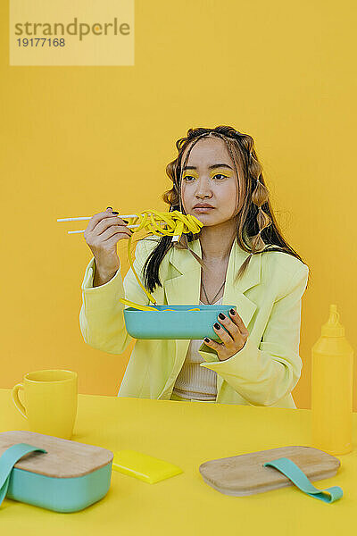 Nachdenkliche Frau isst gelbe Nudeln im Studio