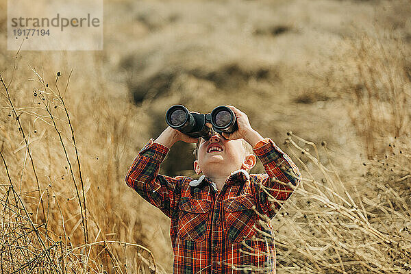 Junge schaut durch ein Fernglas im Weizenfeld
