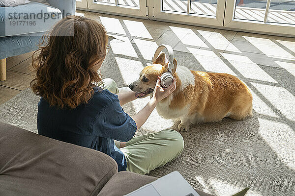 Junge Frau trägt kabellose Kopfhörer  um ihren Hund zu streicheln