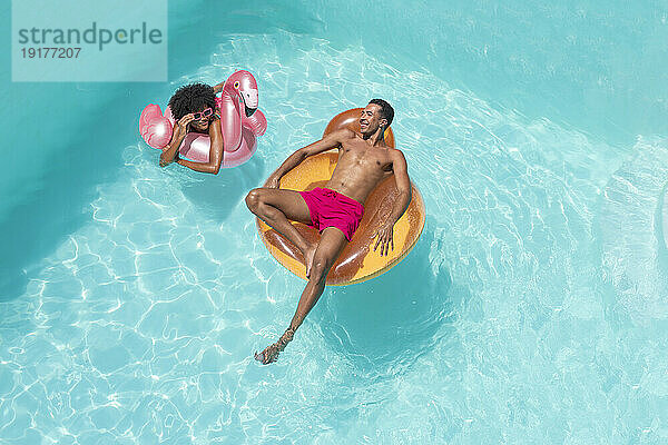 Glücklicher Mann und Frau mit aufblasbarem Schwimmkörper entspannen im Pool