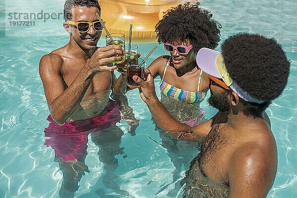 Freunde stoßen an einem sonnigen Tag gemeinsam mit Getränken im Pool an