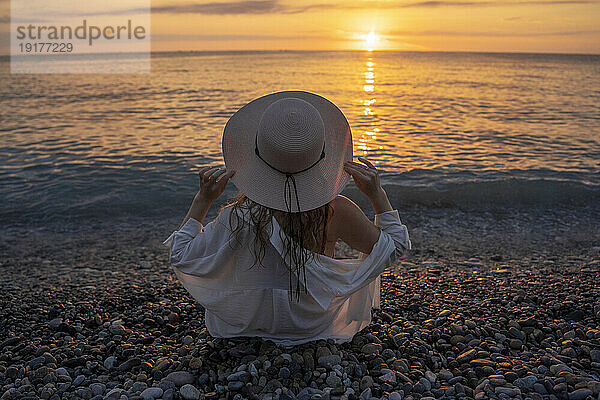 Junge Frau trägt Hut und genießt den Sonnenuntergang am Strand