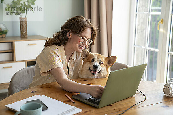 Lächelnder Freiberufler mit Hund  der am Laptop am Tisch arbeitet