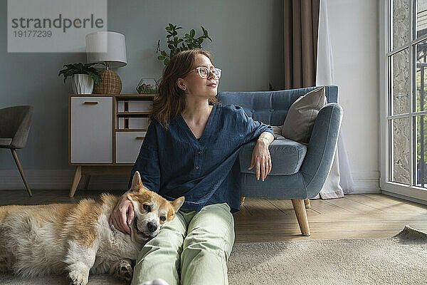 Nachdenkliche Frau sitzt mit walisischem Corgi-Hund im Wohnzimmer