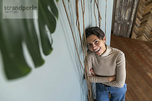 Smiling woman with arms crossed leaning on wall at home