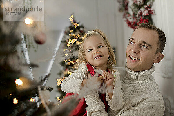 Happy father carrying daughter looking at christmas tree