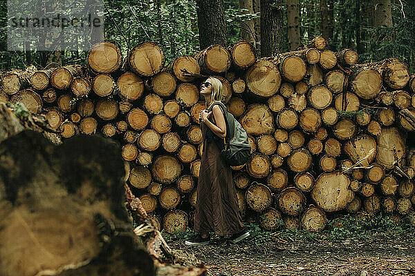 Frau mit Rucksack läuft an Holzstämmen im Wald vorbei