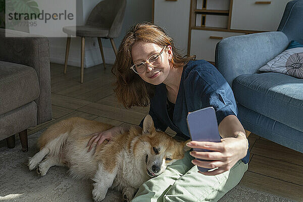 Frau macht zu Hause ein Selfie mit ihrem Hund auf dem Smartphone