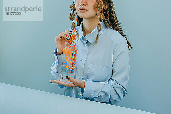 Frau hält Trinkglas mit Quallen und Stroh vor blauem Hintergrund