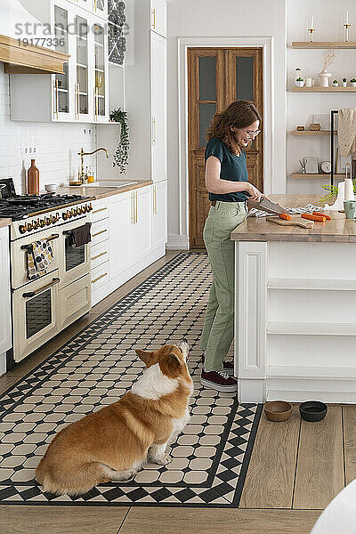 Frau schneidet Karotten mit Hund in der heimischen Küche