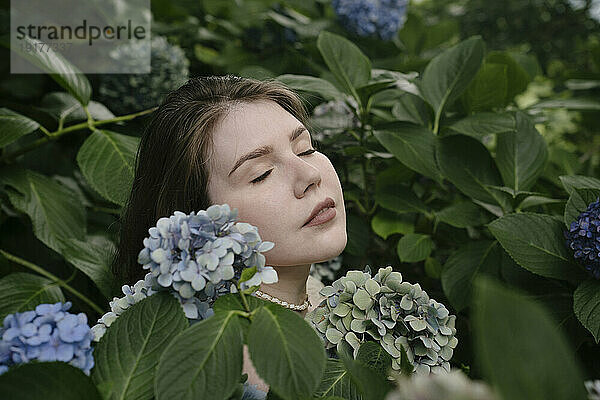 Ruhige Frau mit geschlossenen Augen inmitten von Hortensienblüten