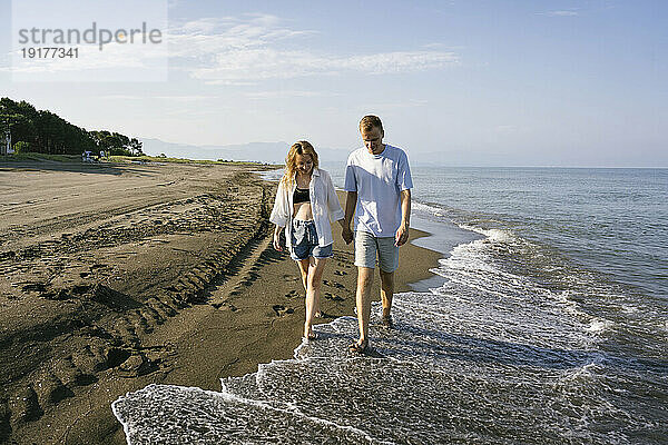 Paar läuft an einem sonnigen Tag barfuß am Strand